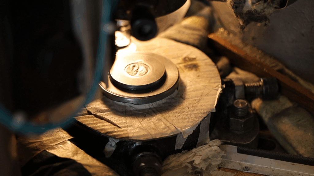 Máquina de estampagem metálica a prensar uma peça com cunhos de aço, produzindo detalhes em relevo com precisão industrial.