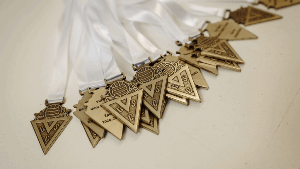 Medalhas desportivas e comemorativas produzidas em zamak, latão ou cobre, combinando técnicas artesanais e industriais para alta qualidade.